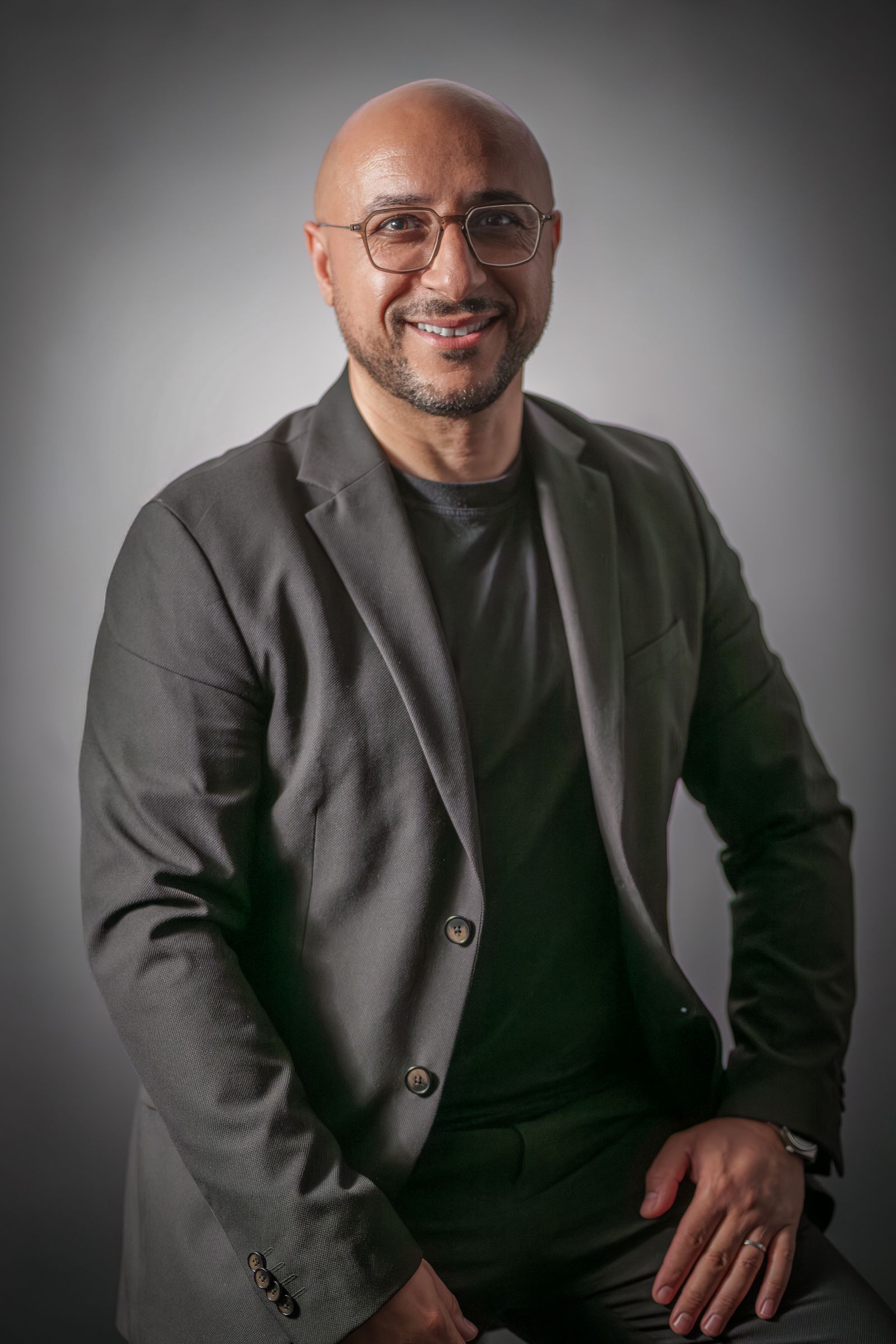 Salim Jebari, souriant, assis en veste sombre sur un fond de studio gris